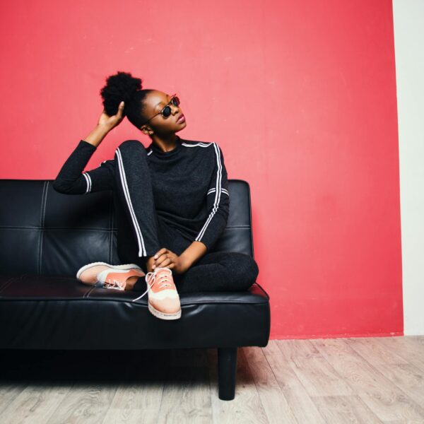 Fashionable young woman in casual wear sitting on a black sofa against a red wall.