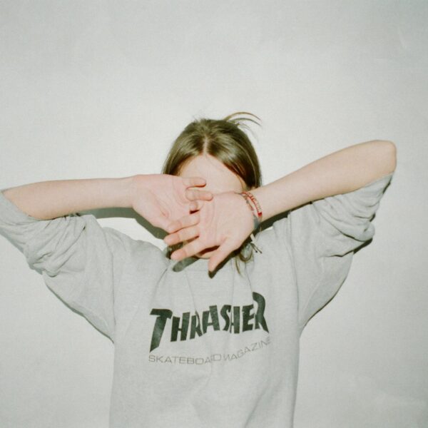 Person wearing a Thrasher sweatshirt covering face, casual and relaxed style.