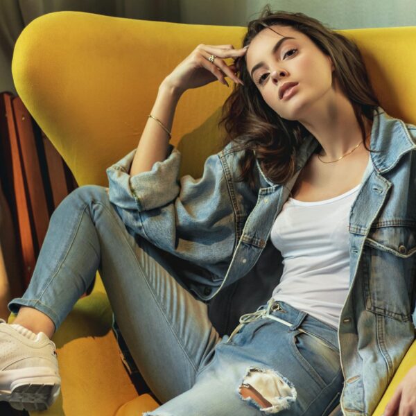 Stylish woman in denim poses on a modern yellow chair indoors.